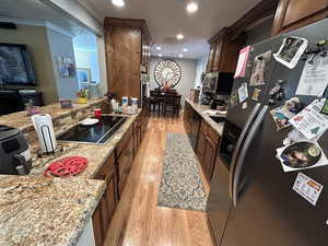 Kitchen featuring light stone counters, light hardwood / wood-style flooring, black appliances, and ornamental molding