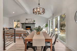 Dining room featuring a brick fireplace, vaulted ceiling with beams, a notable chandelier, and light hardwood / wood-style flooring