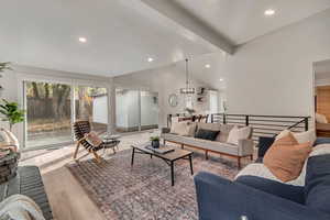 Living room featuring vaulted ceiling with beams, a chandelier, and light hardwood / wood-style floors