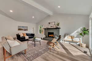 Living room with lofted ceiling with beams, a fireplace, and light hardwood / wood-style flooring