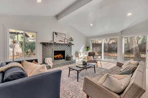 Living room with vaulted ceiling with beams, light hardwood / wood-style floors, and a fireplace