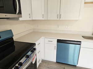 Kitchen with appliances with stainless steel finishes, white cabinets, and light stone countertops