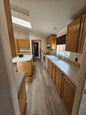 Kitchen with electric stove, vaulted ceiling, sink, light hardwood / wood-style floors, and a center island