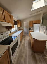 Kitchen featuring lofted ceiling with skylight, hardwood / wood-style floors, white appliances, sink, and a center island