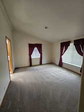 Carpeted spare room featuring ornamental molding and vaulted ceiling