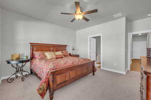 Bedroom with connected bathroom, light colored carpet, and ceiling fan