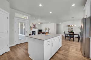 Kitchen featuring stainless steel refrigerator, light wood-type flooring, white cabinets, ceiling fan with notable chandelier, and a center island