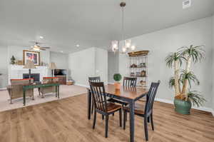 Dining room featuring a tile fireplace, ceiling fan with notable chandelier, and light hardwood / wood-style flooring