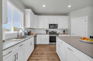 Kitchen with stainless steel appliances, sink, decorative backsplash, light wood-type flooring, and white cabinetry