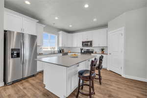 Kitchen with white cabinetry, stainless steel appliances, light hardwood / wood-style flooring, and a center island