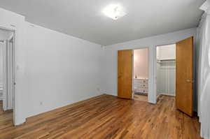 Unfurnished bedroom with hardwood / wood-style flooring, a closet, ensuite bath, and a walk in closet