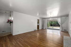 Unfurnished living room featuring hardwood flooring and a notable chandelier