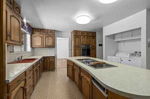 Kitchen with washing machine and clothes dryer, a center island, sink, and black oven