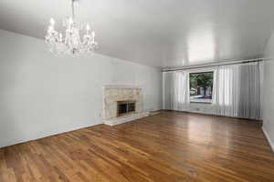 Unfurnished living room with a notable chandelier, a stone fireplace, and hardwood flooring