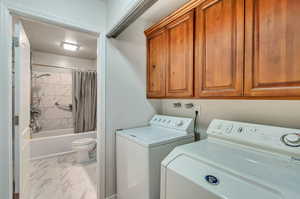 Clothes washing area with cabinets, washer and dryer, and light tile patterned floors