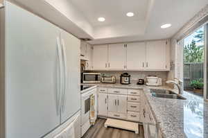 Kitchen featuring white cabinetry, white appliances, sink, a raised ceiling, and dark hardwood / wood-style floors