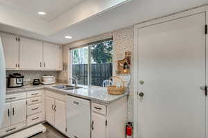 Kitchen with tasteful backsplash, sink, white cabinetry, dishwasher, and wood-type flooring