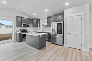 Kitchen featuring appliances with stainless steel finishes, light hardwood / wood-style flooring, sink, a kitchen island, and vaulted ceiling *There are options shown in this photo that would add to the price of the home*