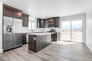 Kitchen with stainless steel appliances, light hardwood / wood-style floors, and dark brown cabinets. *There are options shown in this photo that would add to the price of the home*