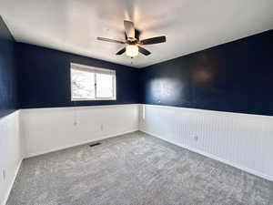 Carpeted empty room with a ceiling fan and a wainscoted wall