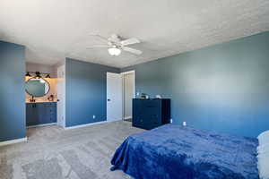 Bedroom with ensuite bath, a textured ceiling, ceiling fan, and light colored carpet