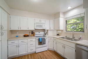 Kitchen featuring white appliances, white cabinets, backsplash, light hardwood / wood-style floors, and sink