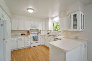 Kitchen with white cabinetry, white appliances, light wood-type flooring, kitchen peninsula, and sink