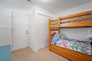 Bedroom with a closet, a textured ceiling, and light colored carpet