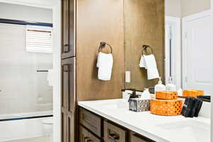 Full bathroom with shower / bath combination with glass door, toilet, and double vanity