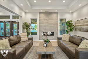 Living room featuring light tile patterned flooring, french doors, a tray ceiling, and a large fireplace