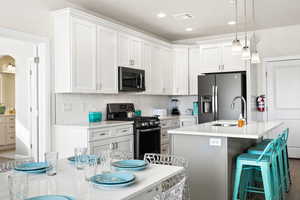 Kitchen featuring stainless steel appliances, sink, backsplash, decorative light fixtures, and an island with sink