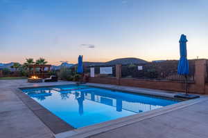 Pool at dusk featuring a mountain view and a patio