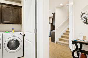 Laundry area with washing machine and dryer, light hardwood / wood-style flooring, and cabinets