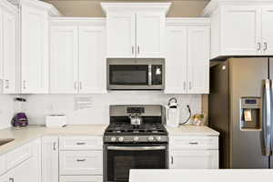 Kitchen with white cabinetry, backsplash, and appliances with stainless steel finishes