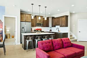 Kitchen featuring a breakfast bar area, a center island, stainless steel appliances, hanging light fixtures, and light carpet