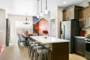 Kitchen with light hardwood / wood-style flooring, stainless steel appliances, hanging light fixtures, dark brown cabinetry, and a kitchen island