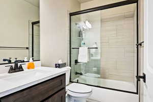 Full bathroom featuring bath / shower combo with glass door, toilet, and vanity