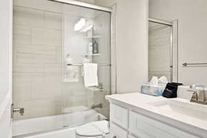 Full bathroom with vanity, shower / bath combination with glass door, and toilet