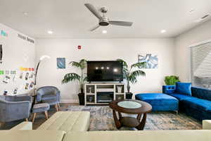 Living room with a fireplace, wood-type flooring, and ceiling fan