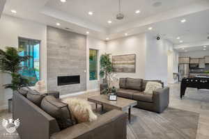 Living room featuring light tile patterned flooring, a stone fireplace, and a tray ceiling