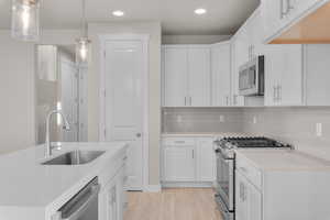 Kitchen featuring white cabinetry, light hardwood / wood-style floors, stainless steel appliances, and decorative light fixtures