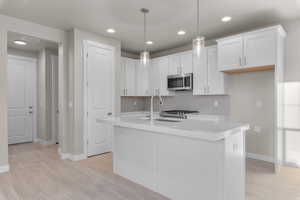 Kitchen featuring stainless steel appliances, sink, a center island with sink, and white cabinets