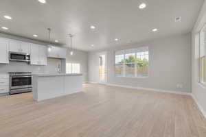 Kitchen featuring an island with sink, stainless steel appliances, pendant lighting, light wood-type flooring, and white cabinets