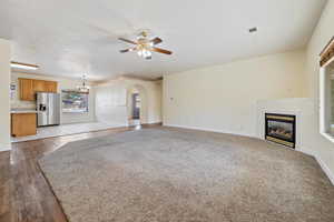 Unfurnished living room with ceiling fan with notable chandelier, light hardwood / wood-style floors, and a textured ceiling