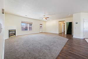 Unfurnished living room featuring ceiling fan, dark hardwood / wood-style floors, and a textured ceiling