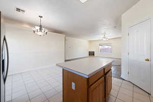 Kitchen featuring light tile patterned flooring, ceiling fan with notable chandelier, decorative light fixtures, a center island, and stainless steel fridge with ice dispenser