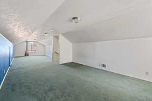 Bonus room with vaulted ceiling, carpet, and a textured ceiling