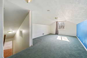 Additional living space featuring vaulted ceiling, a textured ceiling, and dark colored carpet