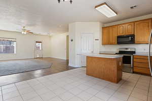 Kitchen with stainless steel electric range, a center island, ceiling fan, and light tile patterned flooring