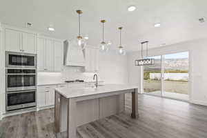 Kitchen featuring light hardwood / wood-style floors, white cabinets, sink, custom range hood, and black microwave